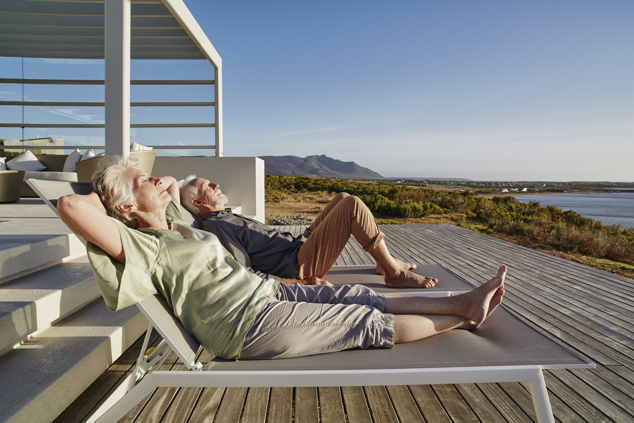 Senior couple lying on deck chairs at luxury beach house